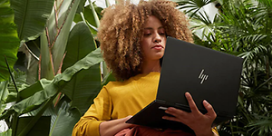 Kvinde står under nogle tropiske planter og holder en HP Envy PC