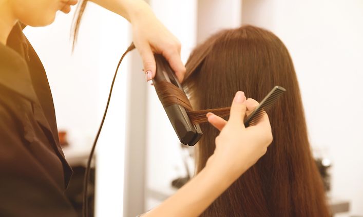 Kvinde med langt brunt hår bliver stylet i salon med glattejern